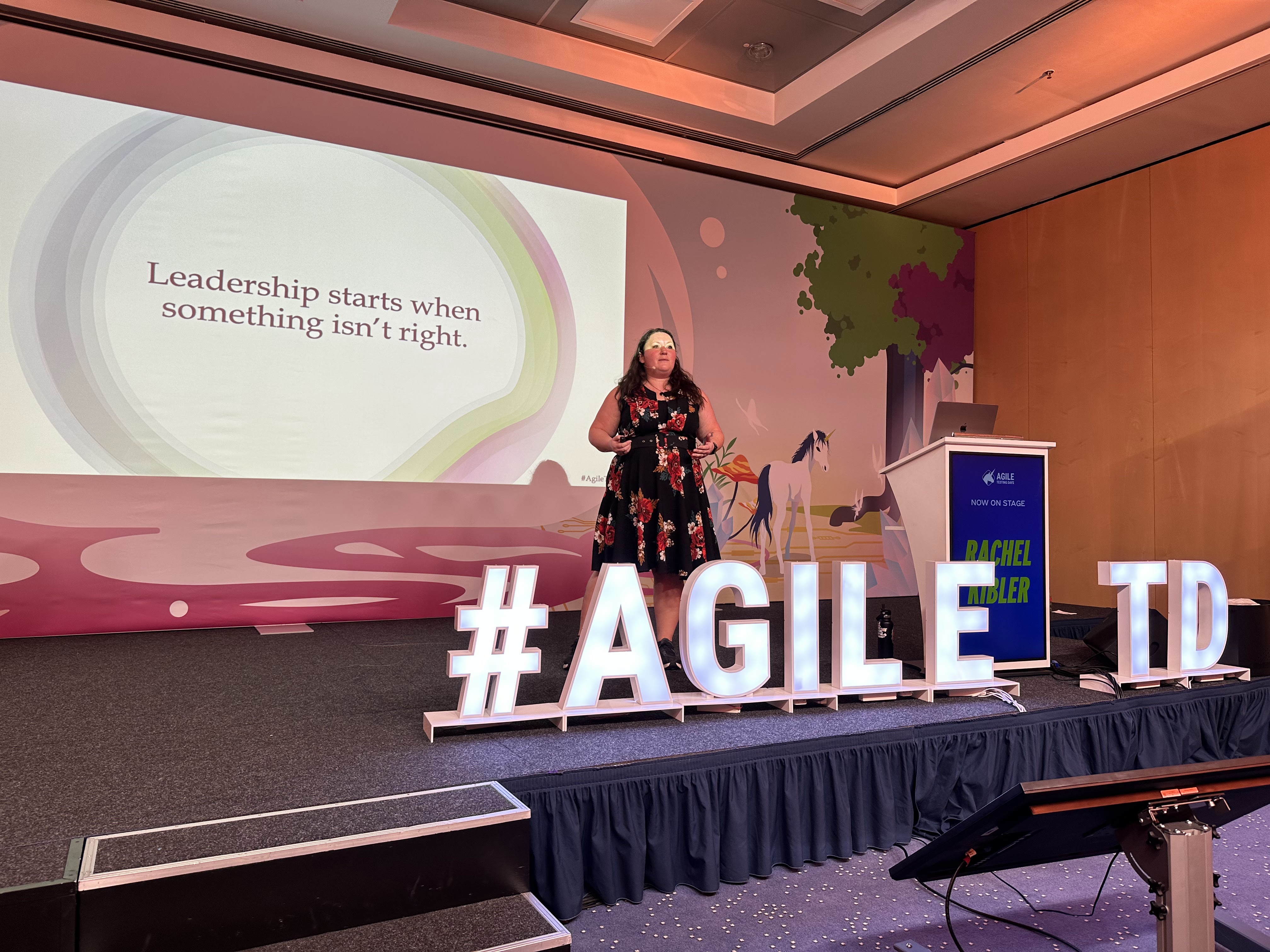 Rachel presenting at Agile Testing Days beside a slide reading “Leadership starts when something isn’t right.”