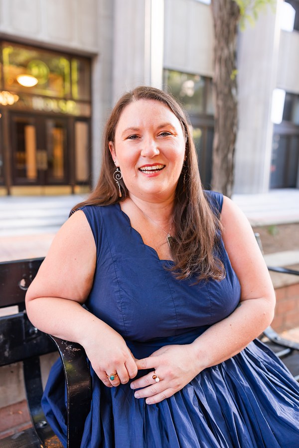 Rachel seated on a bench outdoors, laughing, wearing a navy sleeveless dress