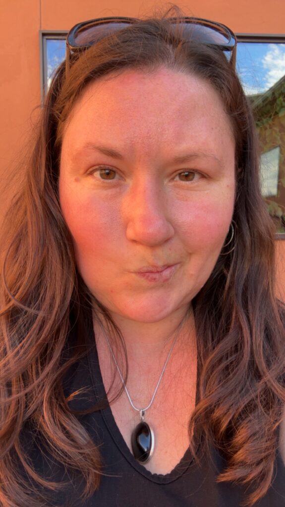 Close-up portrait of Rachel outdoors, hair down, wearing a silver pendant necklace