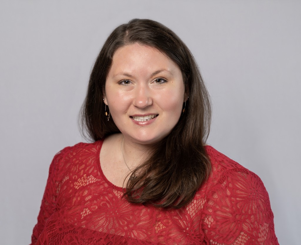 Rachel Joi Kibler, professional headshot, smiling with long dark hair, wearing a red lace top